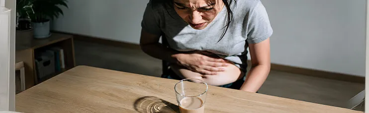 Woman clutching her bloated stomach in discomfort beside a glass of fiber supplement